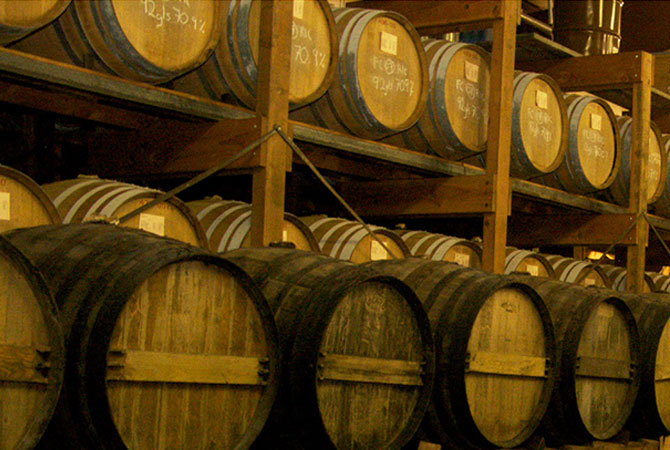 Many oak casks (neatly stacked high) full of aging brandy in Alambic's cellar.
